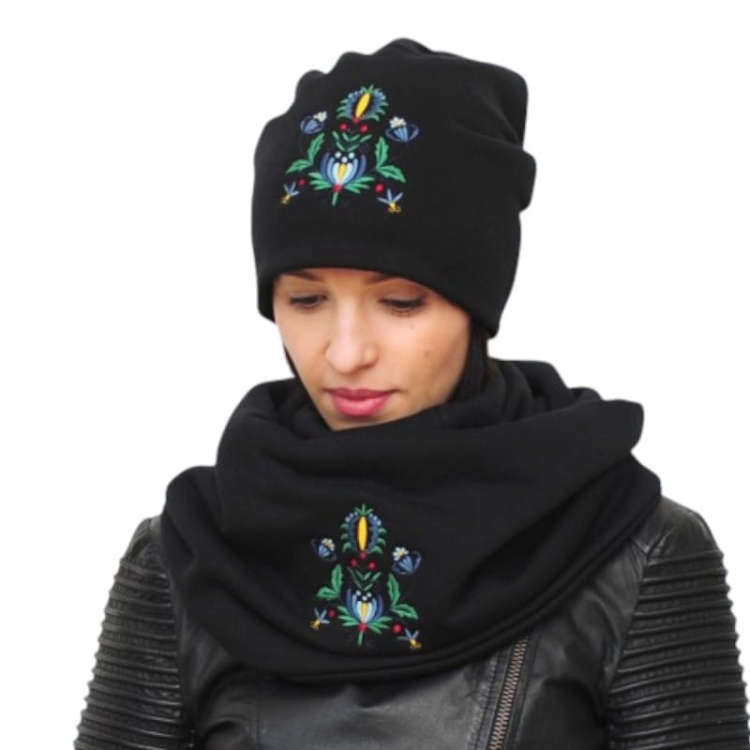 Komplet zimowy z haftem kaszubskim – czapka i komin na białym tle, z wyraźnym folkowym motywem. Kolorowe hafty wyróżniają się na tle jednolitego materiału, dodając uroku i tradycyjnego stylu.